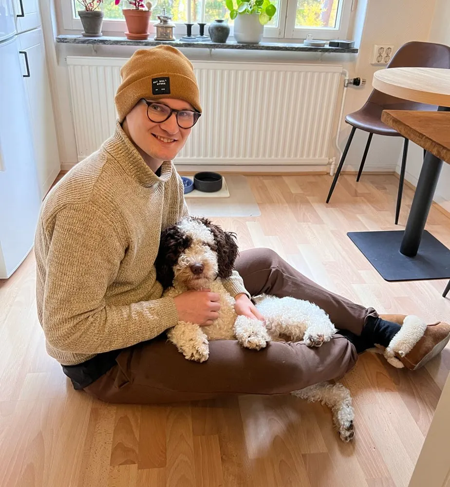 Joakim sitting on the kitchen floor, holding a curly brown and white dog.