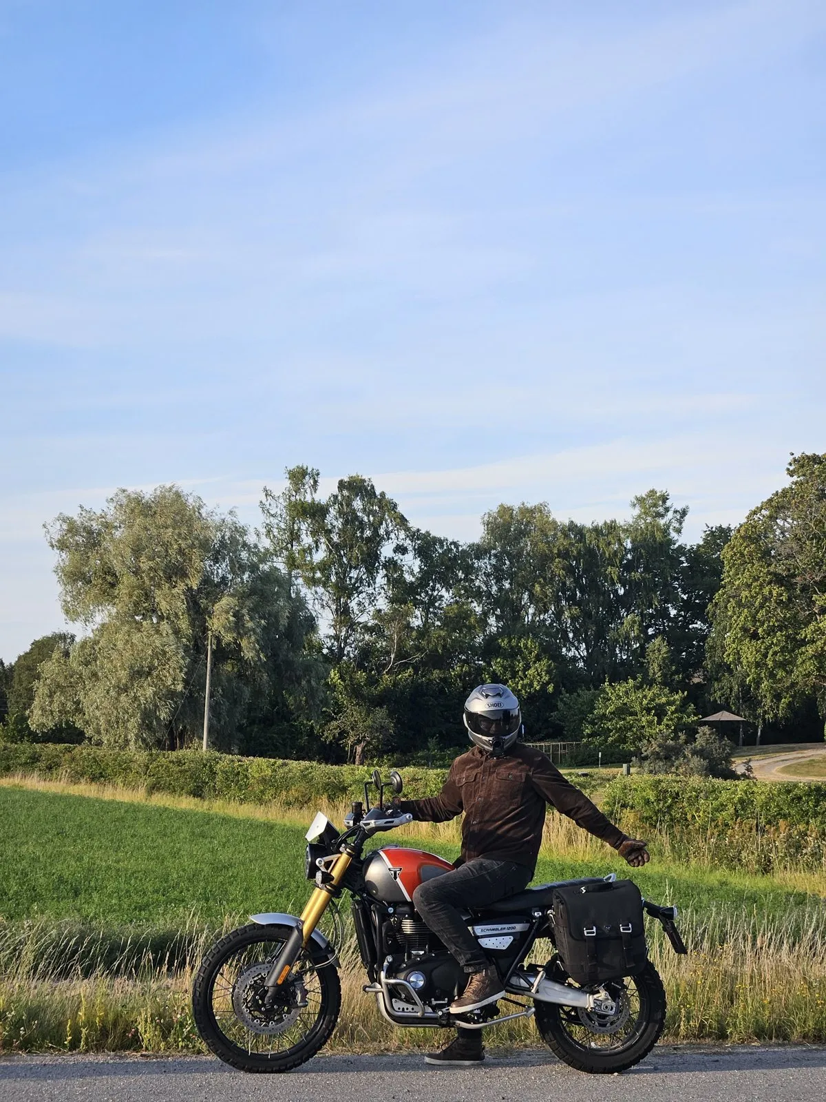 Joakim on a motorcycle on a country road, green fields and trees behind.